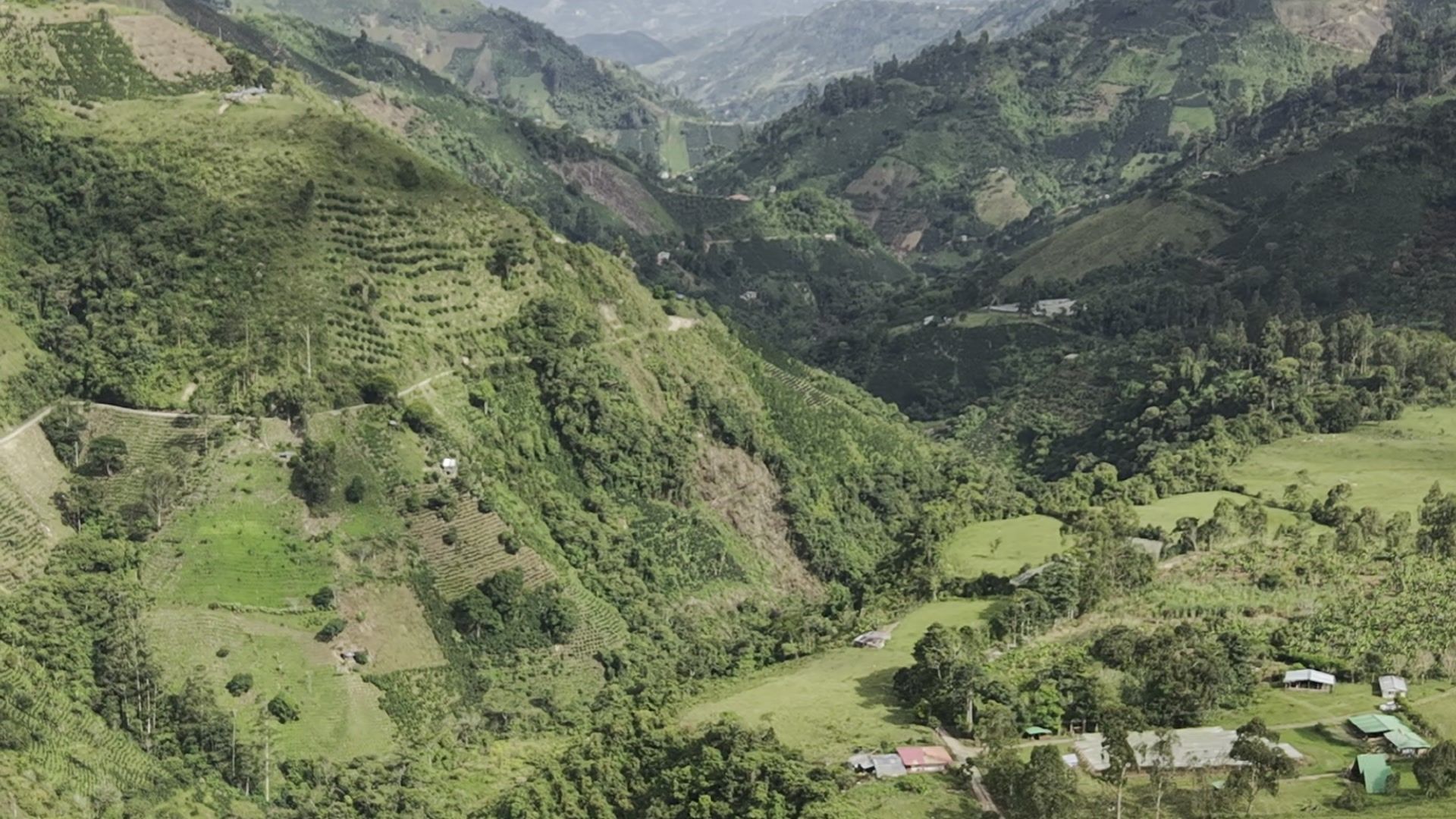 Aerial view of the Vegonia valley: terraced hillsides, a river and farmhouses under layered misty mountains